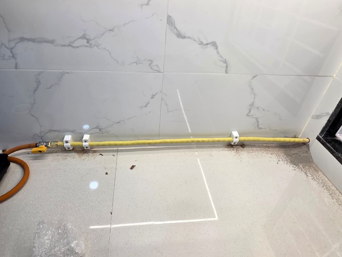 Yellow flexible gas line clamped along a marble backsplash, running from a ball valve to the hob position